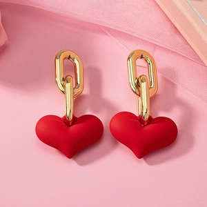 Détail des boucles d'oreilles cœur rouge avec maillons dorés sur fond rose