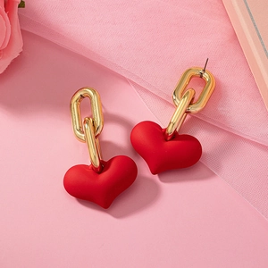 Boucles d'oreilles cœur rouge avec chaîne dorée sur fond floral rose romantique