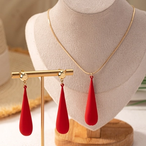 Detalle del conjunto de collar y pendientes de gota roja sobre soporte crema