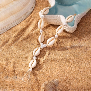 Detail of seashell anklet with pearls on sandy beach background for summer vacation style