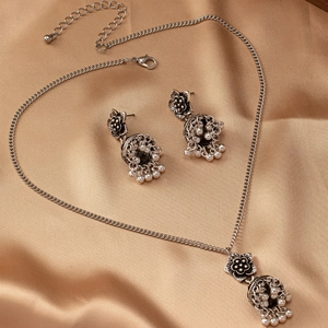 Detail view of retro silver floral necklace and bell earrings on champagne satin