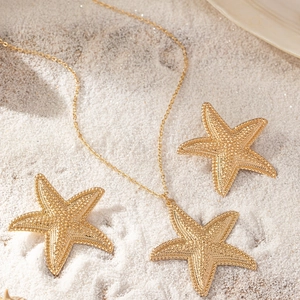 Seestern Schmuckset mit goldener Halskette und Ohrringen auf weißem Sand für den Sommer