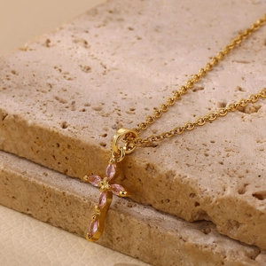 Detalle del colgante de cruz en oro 18K con piedras marquesas rosas sobre travertino