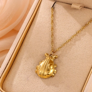 Detailed view of a gold ladybug pendant necklace displayed on beige velvet