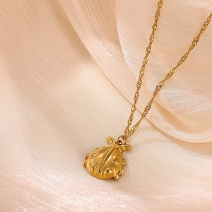 Macro shot of 18k gold plated ladybug pendant on a twisted chain over silk fabric