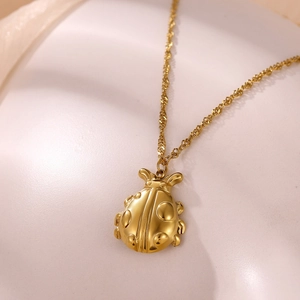 Close-up of a polished 18k gold plated ladybug pendant with delicate water wave chain
