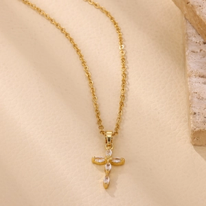 Detalle del colgante de cruz dorada con circonitas marquise en cuero beige