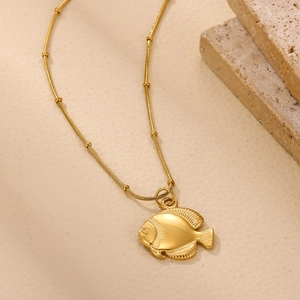 Macro shot of 18k gold plated fish pendant on snake chain with gold beads over sand rock