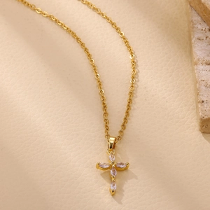 Detalle del colgante de cruz chapado en oro de 18K con circonitas en fondo beige