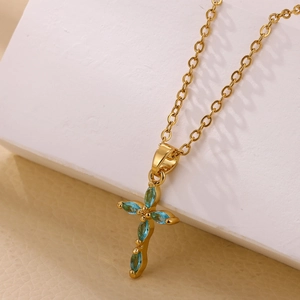 Detalle macro de collar de cruz bañada en oro 18K con piedras turquesas talla marquesa