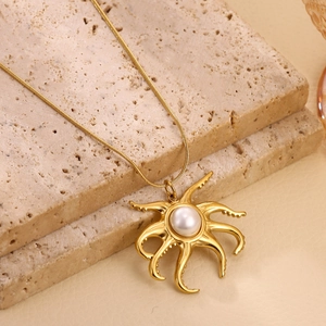 Close-up of golden octopus pendant with large white pearl on a snake chain over stones