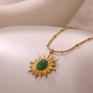 Détail macro du pendentif soleil avec pierre verte sur chaîne en or à perles