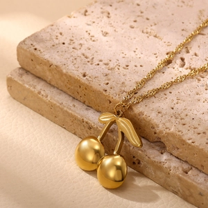 Detail shot of a cherry pendant necklace in 18k gold plating on stone display