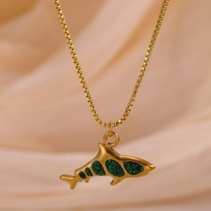 Macro shot of gold shark pendant with sparkling green enamel on a delicate box chain