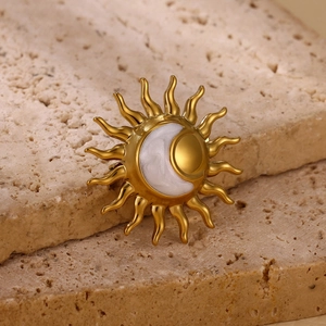 Detailed close-up of a gold-plated sun and moon brooch on a beige textured stone base