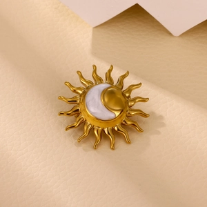 Macro shot of gold sun and moon brooch with shell inlay on a textured beige background