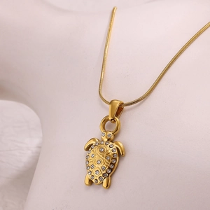 Detail of gold turtle necklace pendant with sparkling rhinestones on a white mannequin