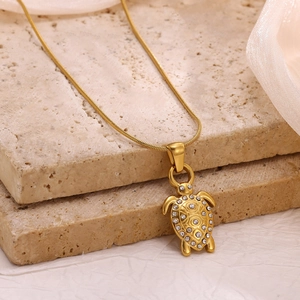 Detailed close-up of 18k gold-plated turtle pendant with sparkling zircon on travertine