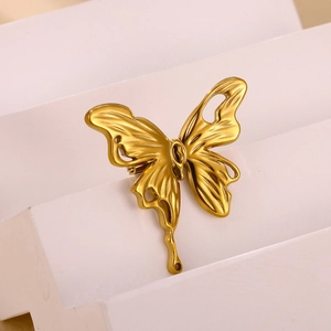 Macro detail of a golden butterfly brooch showing intricate cutout design and matte finish
