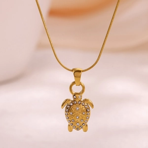 Golden turtle pendant necklace with sparkling crystals and fine snake chain on beige background