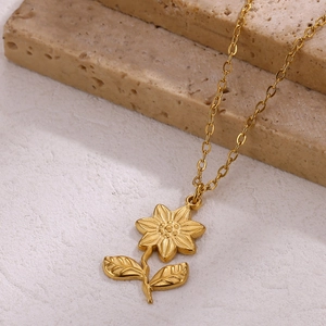 Detail of 18k gold plated sunflower pendant on a cross chain over natural stone