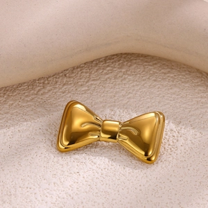 Detail of a polished gold bow brooch on a textured beige stone pedestal in macro view