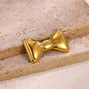 Macro shot of a golden bow brooch featuring mirror-polished finish on beige stone