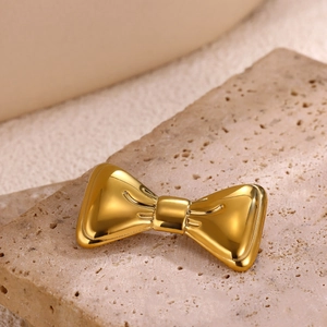 Close-up of a polished gold bow brooch with realistic metal texture on a stone background