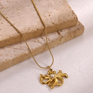 Close-up of gold plated bow pendant necklace with a white pearl on stone slabs