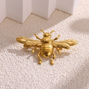 Detailed macro view of a golden bee-shaped brooch with fine textured wings on a white background