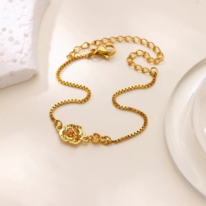 Détail du bracelet chaîne dorée avec pendentif rose 3D et charme de pierre rouge