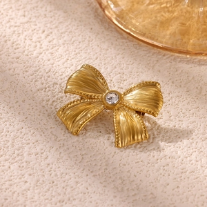 Detail of golden bow brooch with radial brushed texture and center sparkling rhinestone