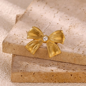 Vintage golden bow brooch with flower details and central zircon on stone background
