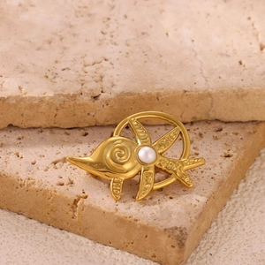 Macro shot of a gold sunfish brooch with pearl inlay on beige natural stone