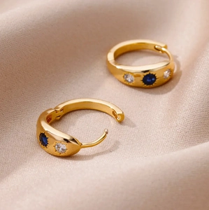 Golden hoop earrings with blue zircon starburst design on champagne silk fabric