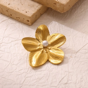 Detailed macro shot of a gold flower brooch featuring a central pearl and brushed texture