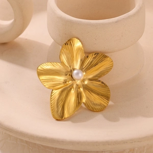 Macro detail of gold-plated sun flower brooch with a central white pearl and brushed texture