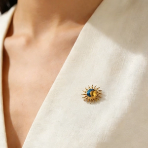 Detail of a vintage sun and moon brooch with gold finish on white linen fabric