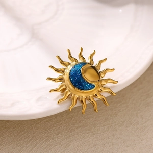 Close-up of a gold sun and moon brooch with blue glitter on a white porcelain plate