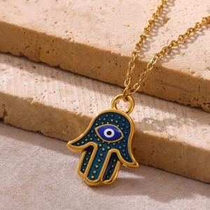 Detailed close-up of a Hamsa hand pendant with a blue evil eye on beige stones