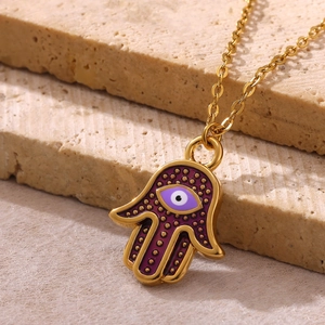 Detailed close-up of gold plated Hamsa hand pendant with purple enamel evil eye on chain