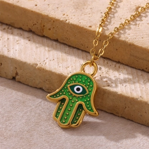 Macro detail of gold Hamsa Hand necklace with green enamel and Evil Eye charm