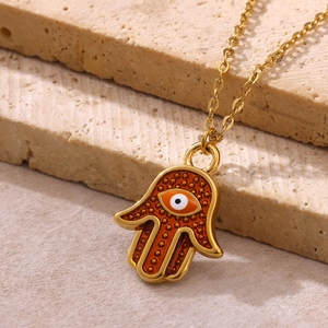 Detail of Hamsa hand pendant with evil eye in gold finish and red enamel on stone