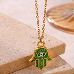 Macro detail of gold-plated Hamsa pendant with green enamel and evil eye motif on stone