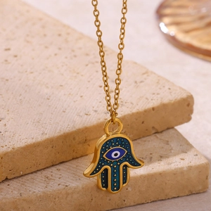 Golden Hamsa Hand necklace with blue Evil Eye pendant on beige travertine stone display