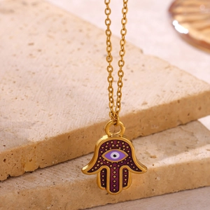 Detail of golden Hamsa Hand pendant with purple enamel and Evil Eye on stone base