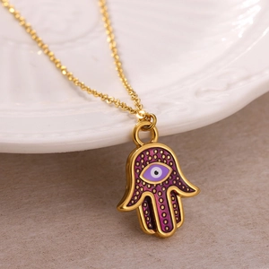 Golden Hamsa Hand necklace with purple enamel and Evil Eye detail on ceramic tray