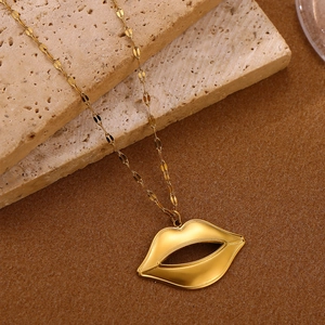 Detail van gouden lipvormige hanger aan een gefacetteerde ketting op beige steen