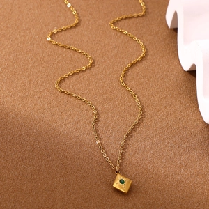 Close-up of bohemian gold necklace with square emerald pendant and textured metal edges