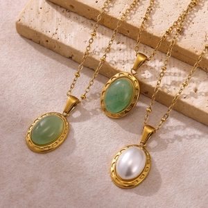 Collier vintage avec pendentif ovale doré, pierre verte et perle sur surface en pierre